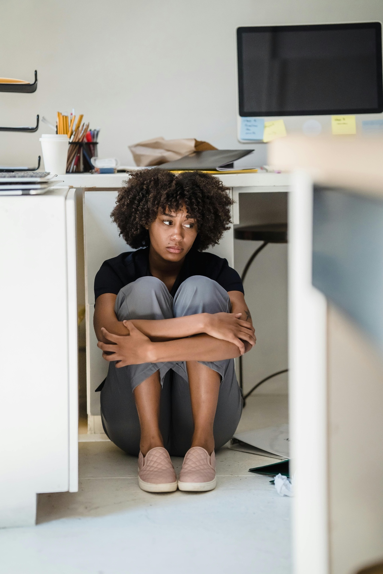 Werknemer zit ineengedoken onder bureau — zinnebeeld van een verstoorde arbeidsrelatie op het werk